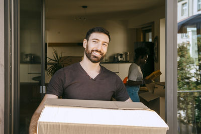 Portrait of smiling man holding cardboard box at doorway of new home