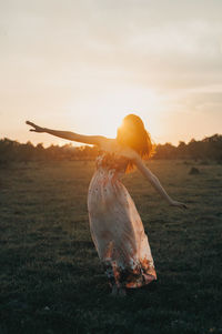 Rear view of woman standing against sky during sunset