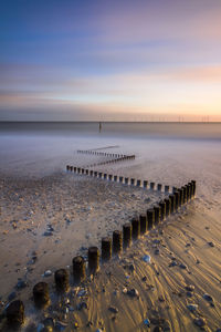 High angle view of wooden posts on beach against sky during sunset