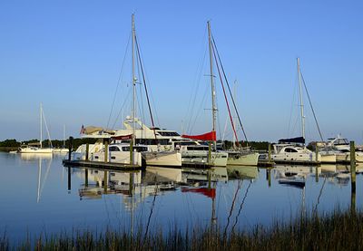 Sailboats moored at harbor against clear blue sky