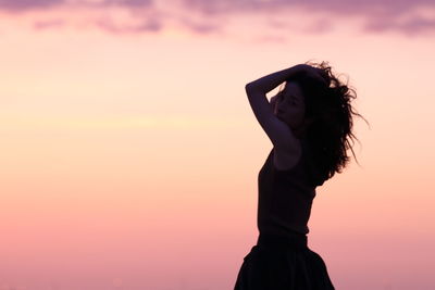 Side view of woman standing against orange sky