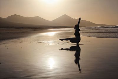 Reflection of silhouette person on beach against sky during sunset