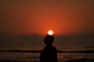 Optical illusion of sun on woman by sea