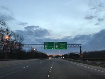 Road sign by trees against sky