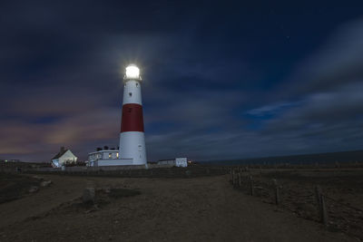 Lighthouse by sea against sky at night