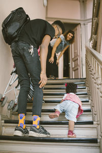 Father and mother looking at baby girl climbing steps in apartment