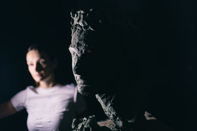 Close-up of sculpture with woman in background in dark