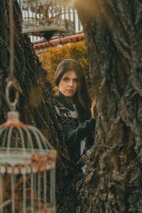 Portrait of young woman standing by tree trunk