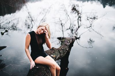 Portrait of woman with hand in hair sitting on fallen tree over lake