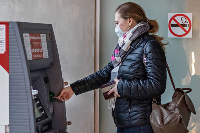 Side view of woman wearing mask using atm