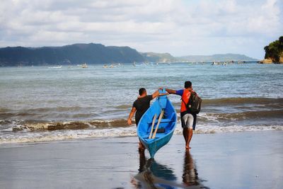 Rear view of men at beach against sky