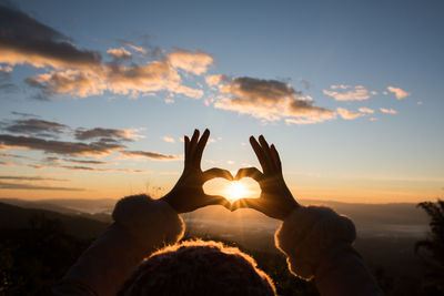 Silhouette hands making heart shape against sky during sunset