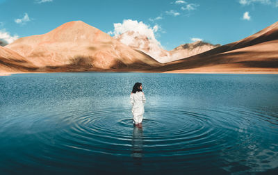 Rear view of woman standing in lake against mountain and sky