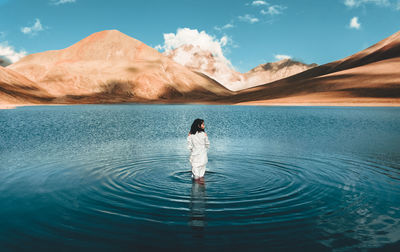 Rear view of man standing in lake against sky