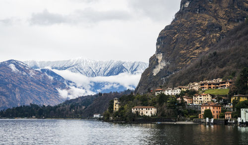 Scenic view of lake by buildings and mountains against sky