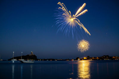 Firework display over sea against sky at night