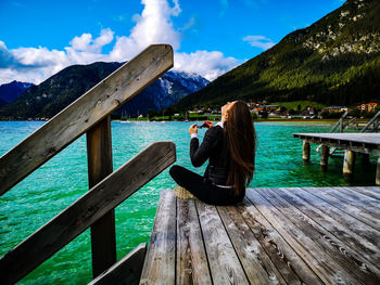 Woman sitting on railing by lake against sky