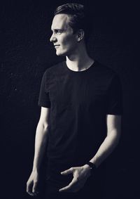 Young man looking away while standing against black background