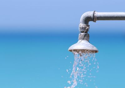 Close-up of water falling from faucet against blue sky