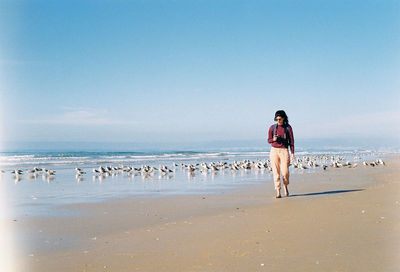 Beautiful woman walking on shore at beach against clear sky