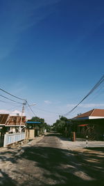 Road by buildings against blue sky