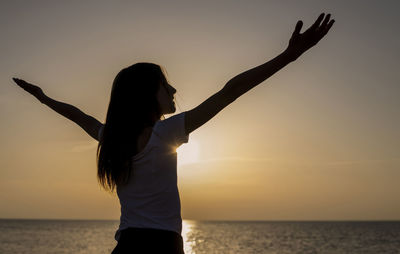 Woman with arms raised on beach against sky during sunset