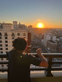 Rear view of kid standing looking out to the sunset and city view 