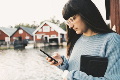 Woman using smart phone while holding digital tablet by lake