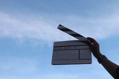 Low angle view of hand holding film slate against sky