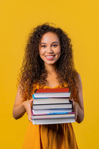 Portrait of smiling young woman against yellow wall