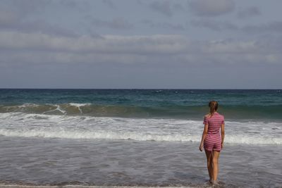 Rear view of woman standing at beach against sky