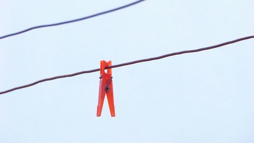 Low angle view of orange clothespin hanging from cable against clear sky