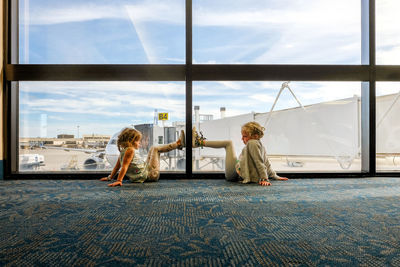 Little girls sitting on ground looking in airport terminal