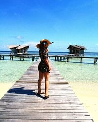 Full length rear view of woman standing on pier at beach