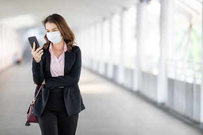 Businesswoman wearing mask using smart phone standing on footbridge