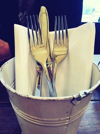 Close-up of cutlery in metal bucket on table