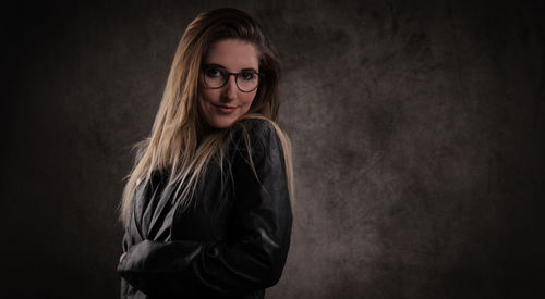 Portrait of young woman standing against black background