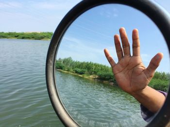 Close-up of hand on lake against sky