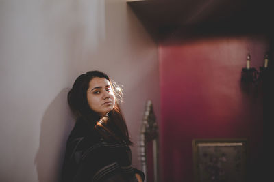 Woman looking away while standing against wall