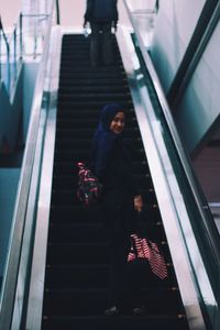 Low angle view of woman wearing hijab standing on escalator