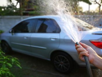 Cropped hand spraying water on car