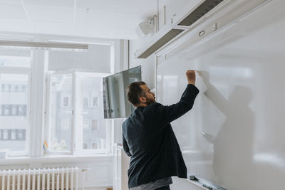 Side view of mature male professor writing on whiteboard in classroom