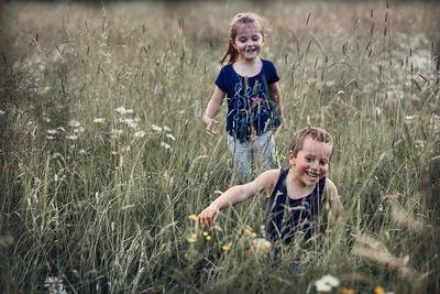 Smiling siblings playing amidst plants on field