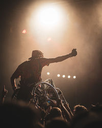 Rear view of man in a wheelchair with arms raised against sky