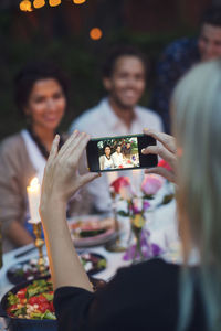 Woman photographing friends through smart phone at garden party