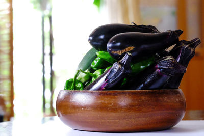 Close-up of eggplants and chili peppers in wooden bowl at table