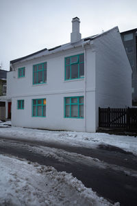 Snow covered houses by building against sky