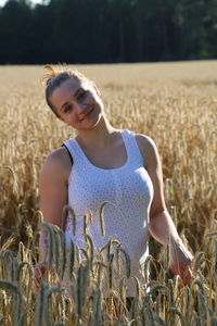 Portrait of smiling young woman standing amidst wheat on farm