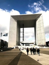 People in front of office building against cloudy sky