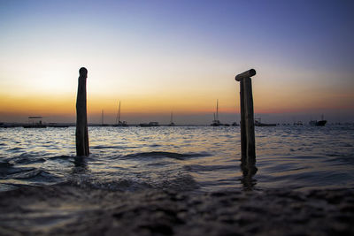 Silhouette wooden post on beach against sky during sunset